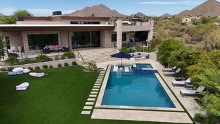 Aerial view of luxury backyard pool with spa, tanning ledge, and desert mountain home