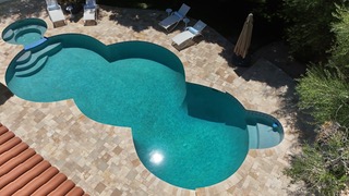 Aerial view of freeform turquoise pool with spa and travertine deck
